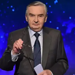 Starsza, siwowłosa osoba w garniturze, która prowadzi jeden z dziesięciu, trzyma okulary i kartkę.